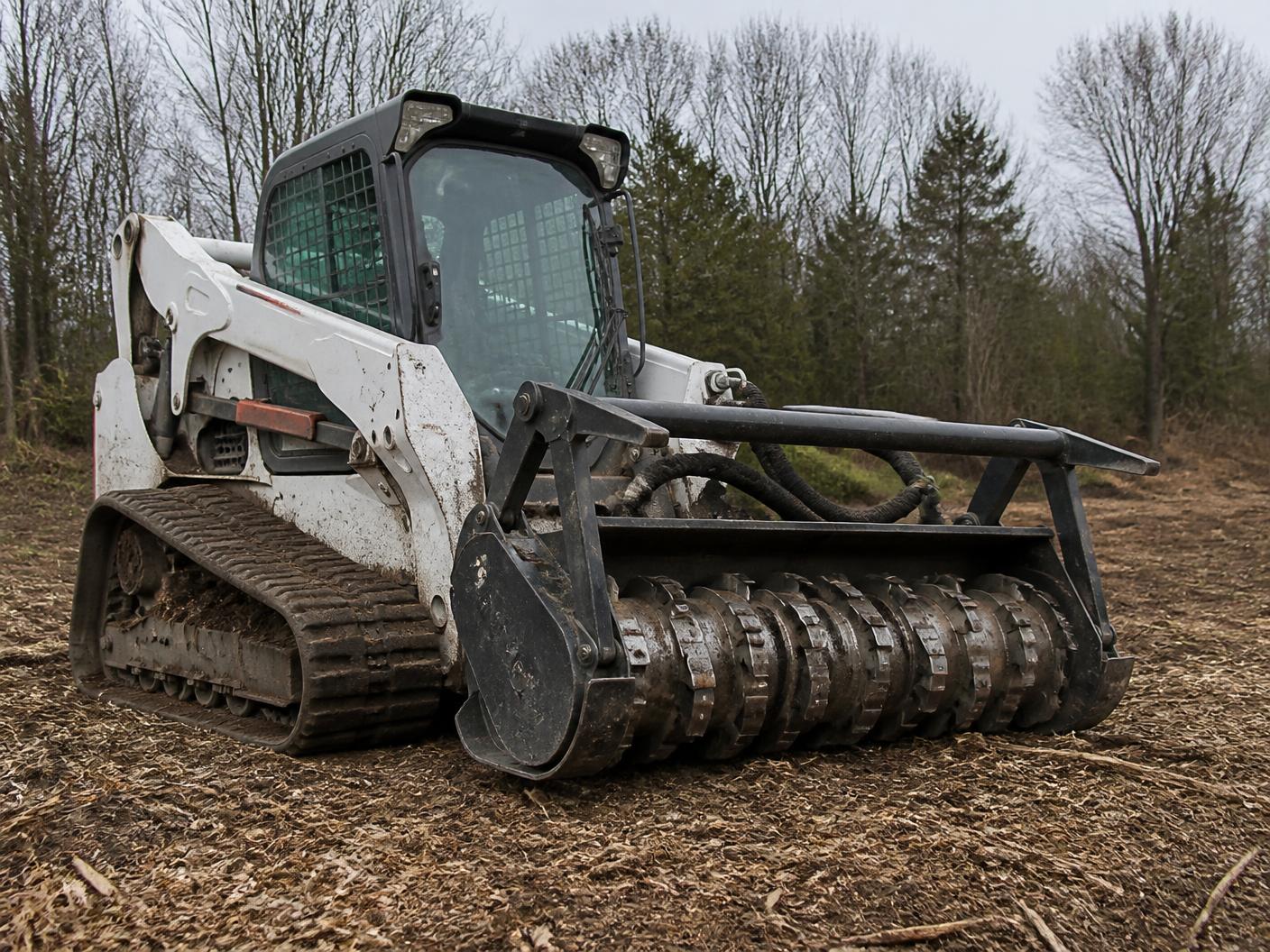 Drum mulching head on a compact track loader resting on freshly cleared ground of a building lot