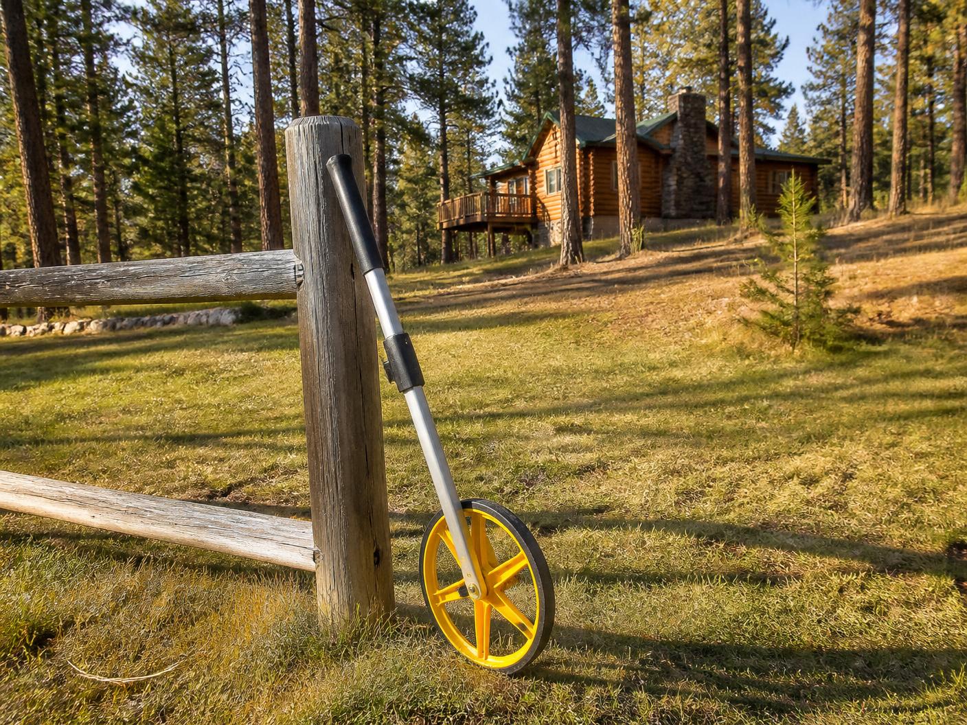 Measuring wheel resting on mown grass against a fence post in the cleared defensible space around a log home